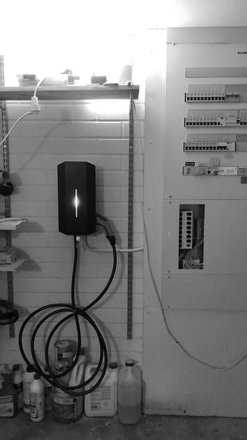 An electric car charger mounted on a garage wall next to the board.